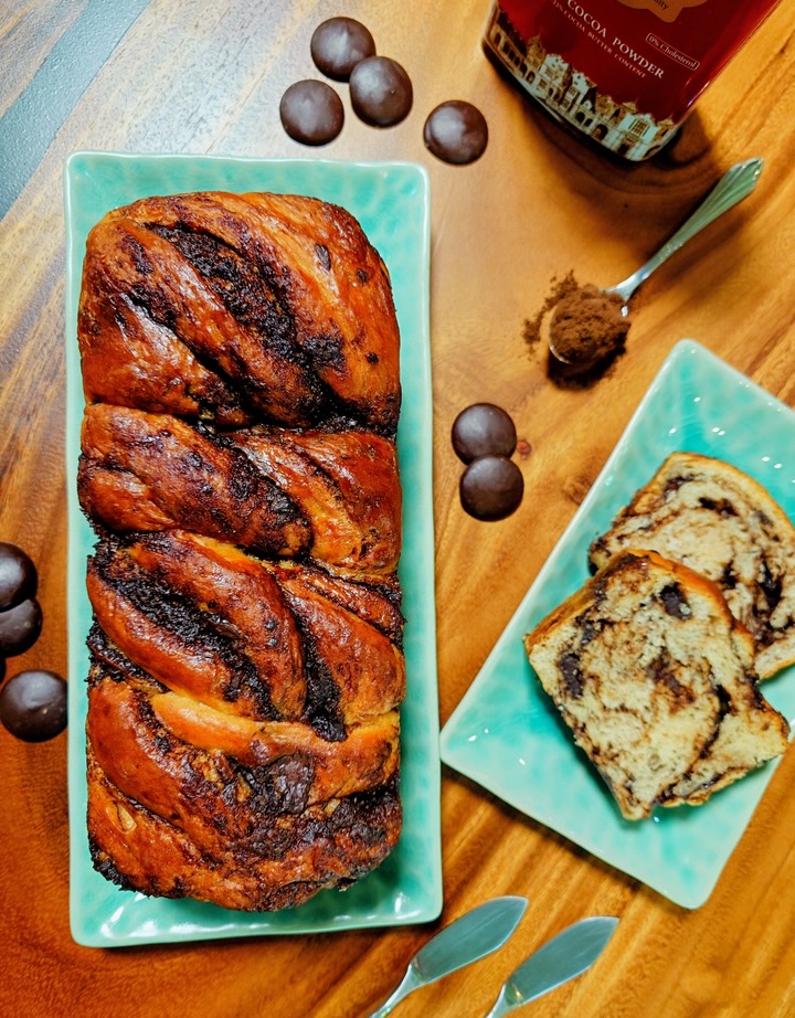 A braided chocolate babka loaf on a turquoise plate with slices and chocolate buttons