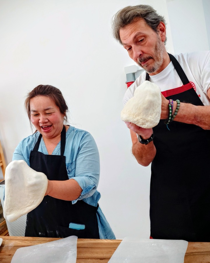 Two class guests laughing as they stretch pizza dough by hand